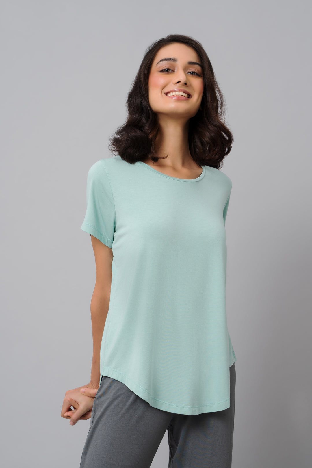 Delicate teal top worn by smiling woman on gray background.