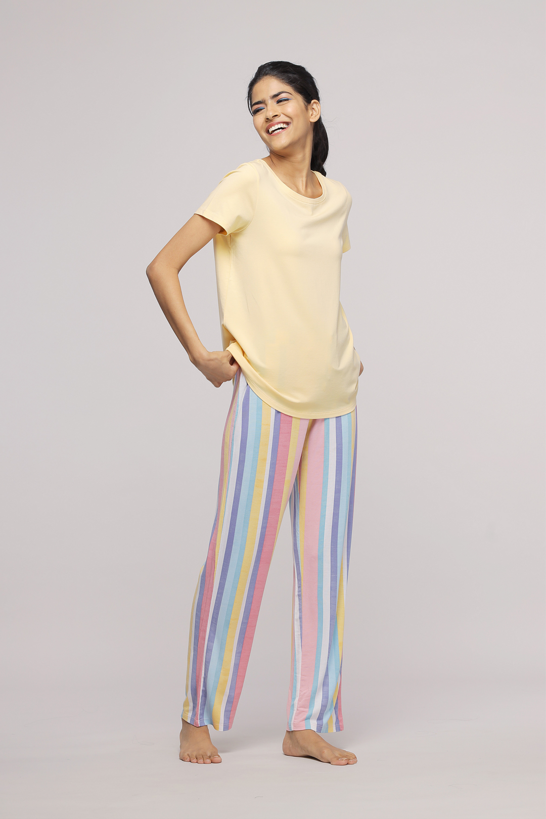 Smiling woman wearing a pastel yellow top with striped pants.